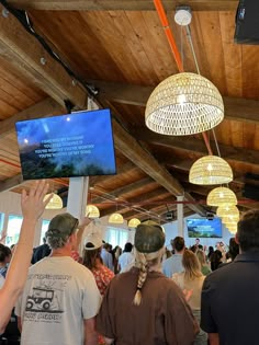 several people are standing in a room with lights hanging from the ceiling and televisions above them