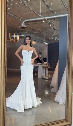 a woman standing in front of a mirror wearing a white dress and posing for the camera