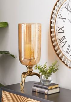 a clock on the wall next to a table with a vase and books in front of it