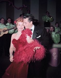 a man in a tuxedo hugging a woman in a red dress and holding a guitar