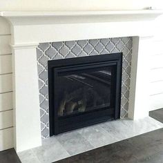 a white fireplace with a black mantle and tile on the wall behind it, in a living room