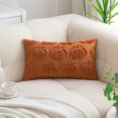 a white couch with an orange pillow on top of it next to a potted plant