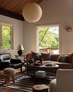 a living room with couches, chairs and tables in front of two large windows