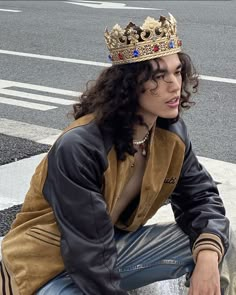 a woman wearing a crown sitting on the ground next to a crosswalk with her hands in her pockets