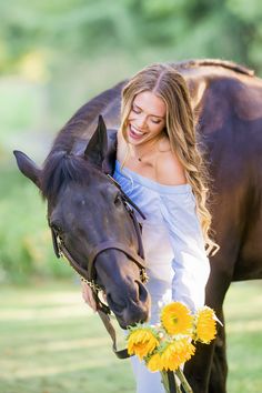 a woman is standing next to a horse with flowers in front of her and smiling at the camera