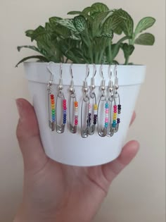 a hand holding a white pot filled with lots of different colored beads and dangling earrings