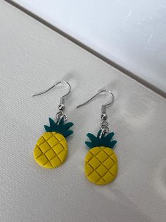 a pair of earrings with pineapples on them sitting on a white table top