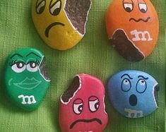 four rocks with faces painted on them sitting next to each other in front of a green cloth