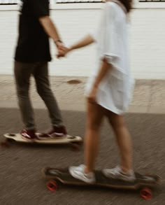 two people are riding skateboards down the street together and one person is holding hands