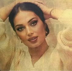 a woman with dark hair wearing a white sweater and holding her hand on her head