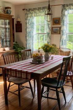 a dining room table with chairs and a checkered tablecloth on it in front of two windows