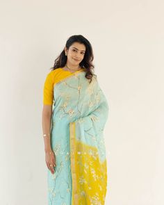 a woman wearing a blue and yellow sari with floral print on the border, standing in