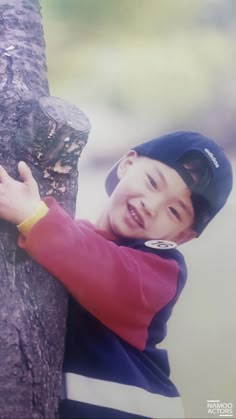 a young boy leans against a tree trunk with his hand on the top of it