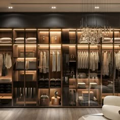 a walk in closet filled with lots of clothes and hanging lights on the wall next to a white chair