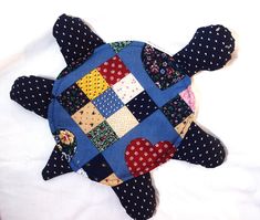 a patchwork turtle pillow is laying on a white sheet with polka dots and hearts