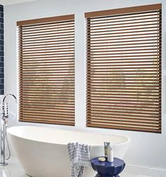 a white bath tub sitting next to two windows with wooden blinds on the window sill