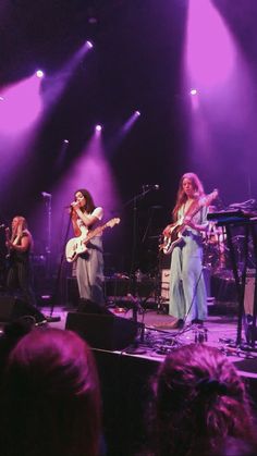 the band is performing on stage with their instruments in hand and purple lighting behind them