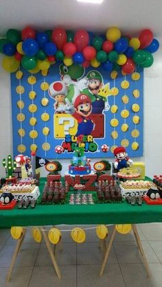 a table topped with lots of cake next to a wall covered in balloons and decorations