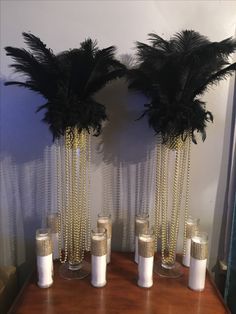 two tall vases with black feathers on top of a wooden table next to candles