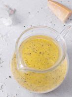 a blender filled with yellow liquid on top of a white counter next to a wooden spoon