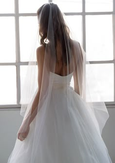 a woman wearing a wedding dress and veil in front of a window with sunlight streaming through it