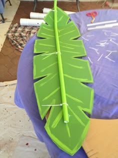 a large green leaf sitting on top of a purple tablecloth covered floor next to scissors