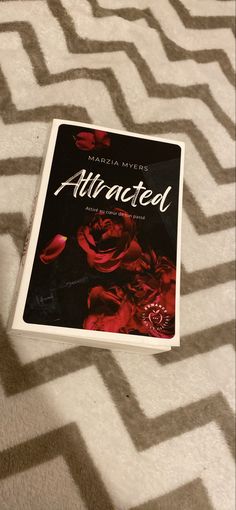 a book sitting on top of a bed next to a white and black rug with red flowers