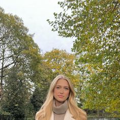 a woman standing in front of trees with her hands on her hips and looking at the camera