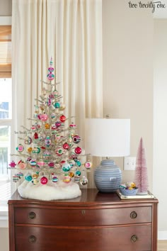 a white christmas tree sitting on top of a wooden dresser in front of a window