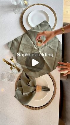 a person is setting a table with napkins and place settings on it, while another person holds a wine glass in their hand