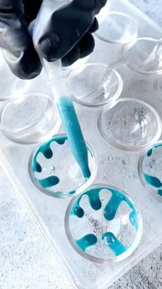 a person in black gloves pouring blue liquid into cups