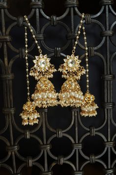 A traditional masterpiece, replete with traditional grandeur and an opulent design, these earrings are richly encrusted kundan jhumkas. The long hair chain with dangling trinkets of pearl suffuses the design with charm. Closure - Push-Back Style Tip - When it comes to getting a classic look, nothing can be better than pearls and kundan. This necklace set is fit for a woman who is fiercely independent yet rooted in traditional and cultural heritage, carving her own style with classic and timeless Heavy Traditional Kundan Jhumkas, Traditional Kundan Jhumkas For Festive Occasions, Traditional Kundan Jhumkas For Festivals, Traditional Tilla Jhumkas For Eid, Traditional Jhumkas For Eid Festivities, Traditional Jhumkas For Eid Festival, Festive Gota Work Jhumkas For Eid, Festive Kundan Jhumkas With Latkans, Traditional Kundan Jhumkas For Navratri