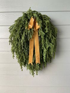 a wreath hanging on the side of a building with gold ribbon and evergreen leaves around it