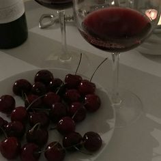 some cherries are on a plate next to a glass of wine