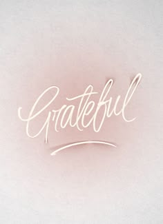 the word grateful written in cursive writing on a white paper with a pink background