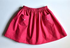 a pink skirt with buttons on the side and pockets at the bottom, sitting on a white surface