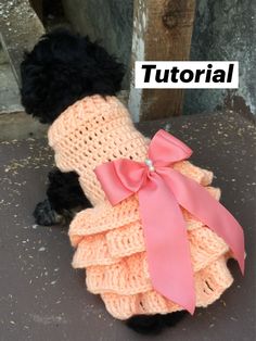 a small black dog wearing a dress made out of knitted material with a pink bow