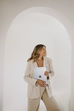 a woman holding a laptop in her right hand and smiling at the camera while standing next to an archway