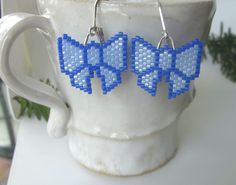 "Be the present with these blue ribbon bows on each side of your face! These adorable blue bows with sparkling darker blue accents are wonderful gifts for any occasion. Exciting and trendy, these earrings will enhance any outfit and will bring many compliments. These earrings are so light that they dance and sparkle with every move you make. Handmade with tiny Miyuki Delica beads they are as unique as they are cute. The sterling silver lever back closures mean you don't have to worry about them slipping out of your earlobe. The dangle's length and the bow's width are close to 1\". AND they are available in several solid colors." Cute Light Blue Earrings For Gift, Cute Light Blue Earrings Gift, Light Blue Beaded Earrings With Ear Wire As Gift, Light Blue Beaded Earrings Gift, Light Blue Beaded Earrings As Gift, Handmade Light Blue Beaded Earrings For Gift, Blue Ribbon Bow, Beaded Bow, Cute Gifts For Her