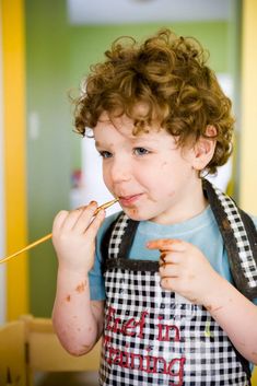 a young boy is eating something with a stick in his mouth while wearing an apron