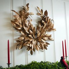 a metal wreath is hanging on the wall next to some red candles and greenery