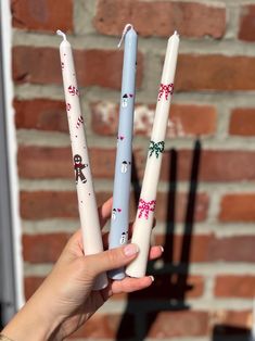 three candles with christmas decorations on them are held in front of a brick wall and window