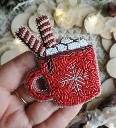 a hand holding a red and white beaded coffee cup brooch with candy canes on it