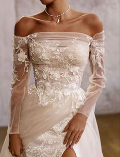 a woman in a wedding dress with sheer sleeves and flowers on the skirt is posing