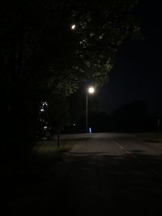 an empty road at night with street lights lit up on either side and trees in the background