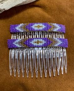 three purple and white beaded combs sitting on top of a brown cloth covered surface