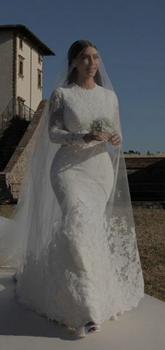 a woman in a white wedding dress and veil walking down the street with her hand on her hip