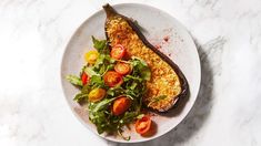 a white plate topped with an eggplant covered in cheese and tomatoes next to a salad