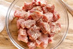 a glass bowl filled with meat sitting on top of a wooden table next to a napkin