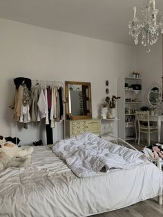 an unmade bed sitting in a bedroom next to a chandelier and dresser